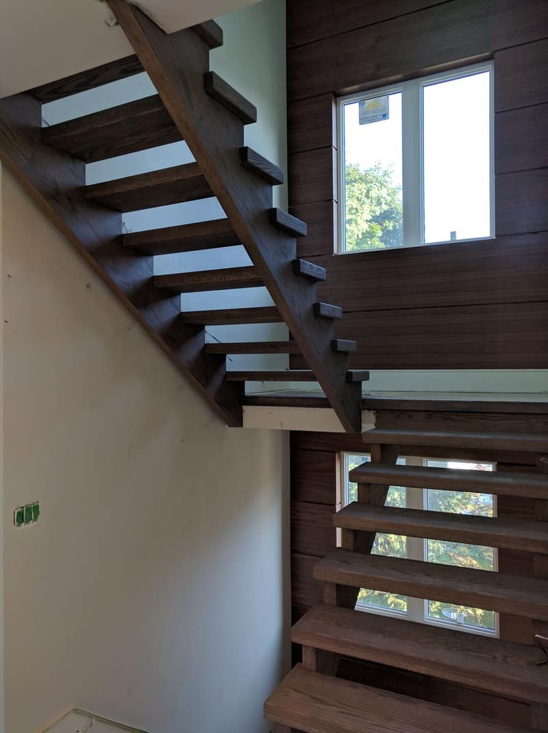 Open-riser floating staircase in dark-stained hardwood during construction